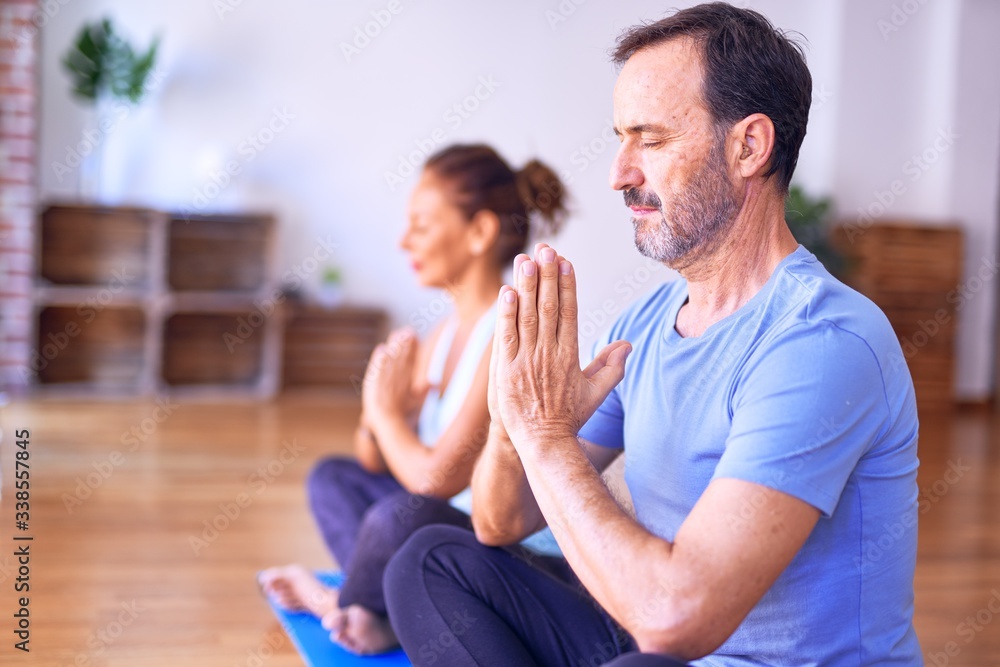 Middle age beautiful sporty couple sitting on mat practicing yoga doing prayer pose at gym Middle age beautiful sporty couple sitting on mat practicing yoga doing prayer pose at gym