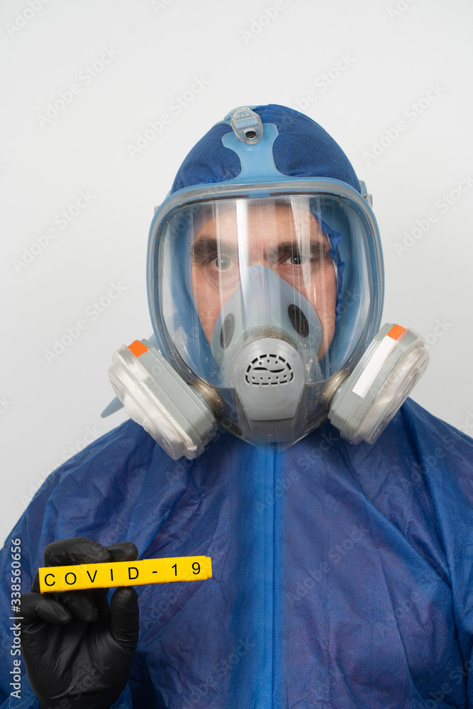 a man in a protective suit and mask holds a sign that reads covid 19