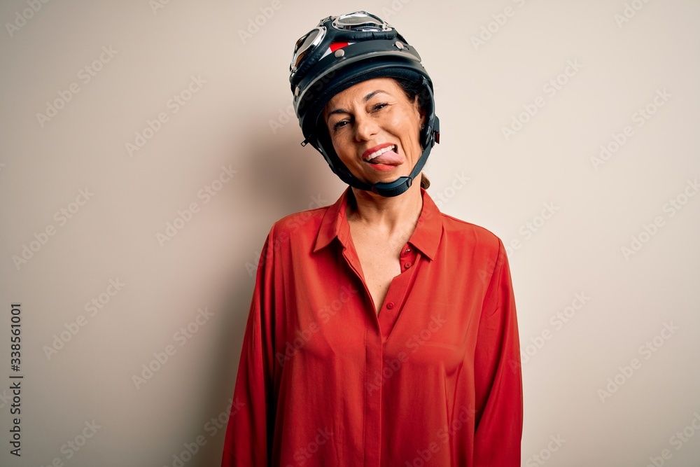 Middle age motorcyclist woman wearing motorcycle helmet over isolated white background sticking tongue out happy with funny expression. Emotion concept. Middle age motorcyclist woman wearing motorcycle helmet over isolated white background sticking tongue out happy with funny expression. Emotion concept.