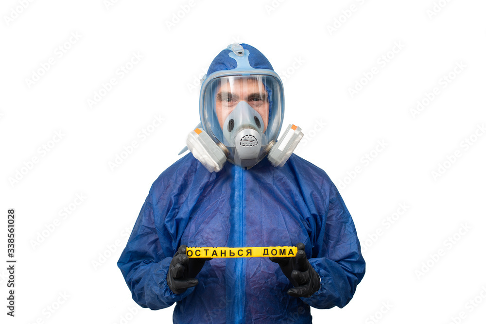 a man in a protective blue suit and a protective mask holds a sign stay at home