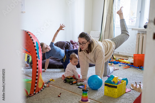 Mother making workout in messy nursery with kids around. Family lifestyle concept. Home workout social distancing self isolation