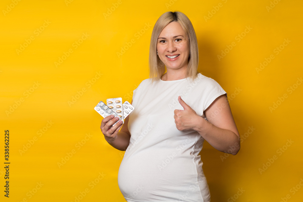 happy pregnant woman, blonde makes a thumbs-up gesture while holding the pills. safe medications for pregnancy happy pregnant woman, blonde makes a thumbs-up gesture while holding the pills. safe medications for pregnancy