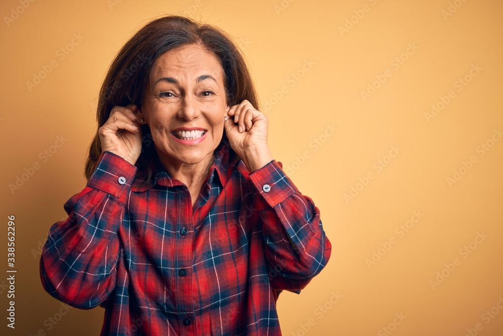 Middle age beautiful woman wearing casual shirt standing over isolated yellow background Smiling pulling ears with fingers, funny gesture. Audition problem Middle age beautiful woman wearing casual shirt standing over isolated yellow background Smiling pulling ears with fingers, funny gesture. Audition problem