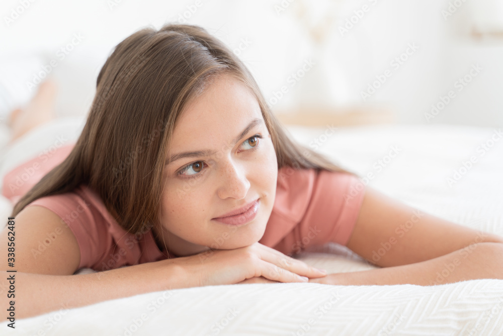 Close-up of young dreamy brunette girl, lying on white bed, looking aside as if thinking of future plans or date with her boyfriend Close-up of young dreamy brunette girl, lying on white bed, looking aside as if thinking of future plans or date with her boyfriend