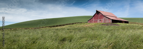 Cuadro en lienzo a panorama of green fields and a fence leading to an old red barn