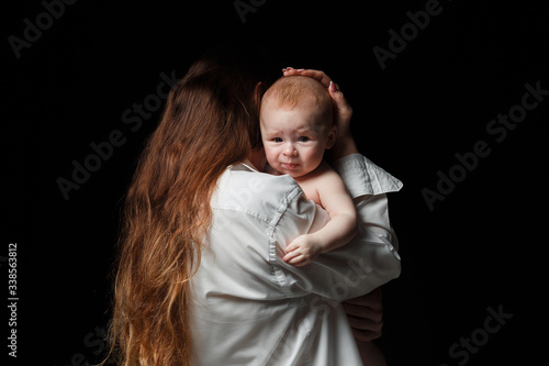 mother brunette with long hair and a white shirt is standing with her back and holding a newborn son. black background.