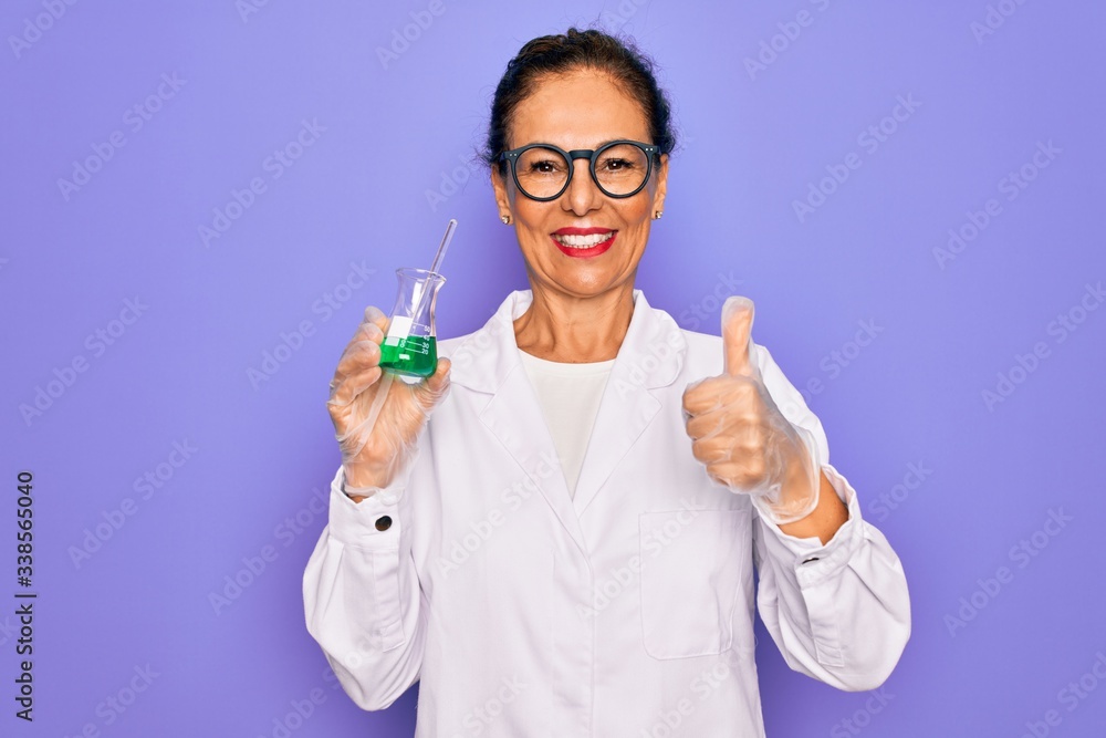 Middle age senior scientist woman wearing laboratory coat holding research test tube happy with big smile doing ok sign, thumb up with fingers, excellent sign Middle age senior scientist woman wearing laboratory coat holding research test tube happy with big smile doing ok sign, thumb up with fingers, excellent sign
