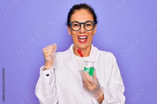 Middle age senior scientist woman wearing laboratory coat holding research test tube screaming proud and celebrating victory and success very excited, cheering emotion
