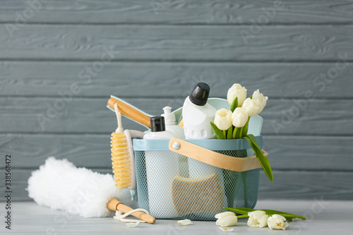 Set of cleaning supplies and spring flowers on grey wooden background