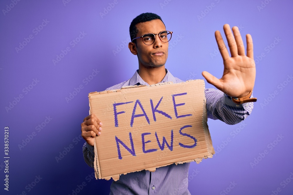 Young handsome african american man protesting holding banner with fake ...