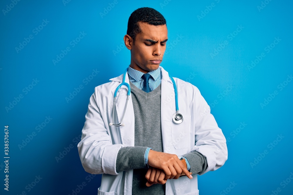 Handsome african american doctor man wearing coat and stethoscope over blue background Checking the time on wrist watch, relaxed and confident Handsome african american doctor man wearing coat and stethoscope over blue background Checking the time on wrist watch, relaxed and confident