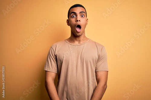 Young handsome african american man wearing casual t-shirt standing over yellow background afraid and shocked with surprise and amazed expression, fear and excited face.