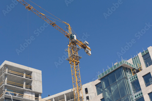Building crane and building under construction against blue sky. Industry