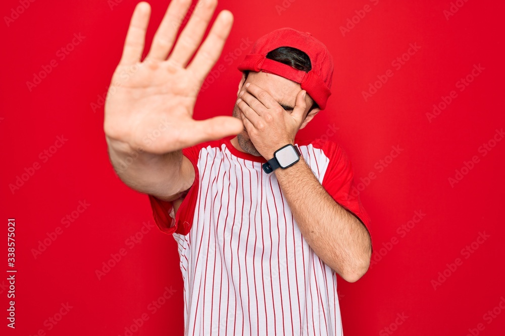 Young handsome sporty man with blue eyes wearing striped baseball t-shirt and cap covering eyes with hands and doing stop gesture with sad and fear expression. Embarrassed and negative concept.