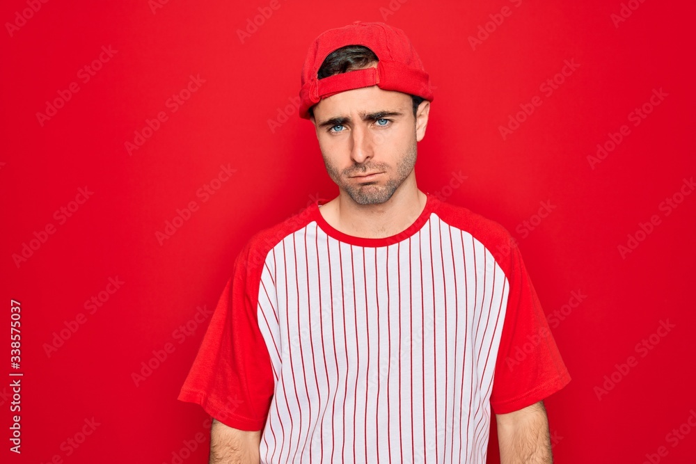 Young handsome sporty man with blue eyes wearing striped baseball t-shirt and cap depressed and worry for distress, crying angry and afraid. Sad expression.