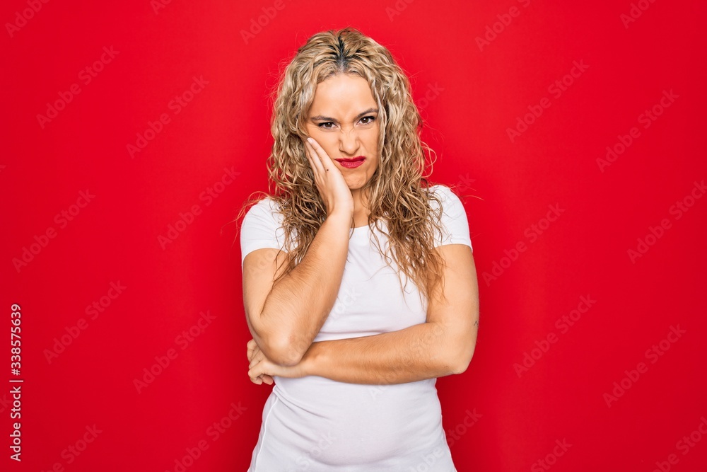 Young beautiful blonde woman wearing casual t-shirt standing over isolated red background thinking looking tired and bored with depression problems with crossed arms. Young beautiful blonde woman wearing casual t-shirt standing over isolated red background thinking looking tired and bored with depression problems with crossed arms.