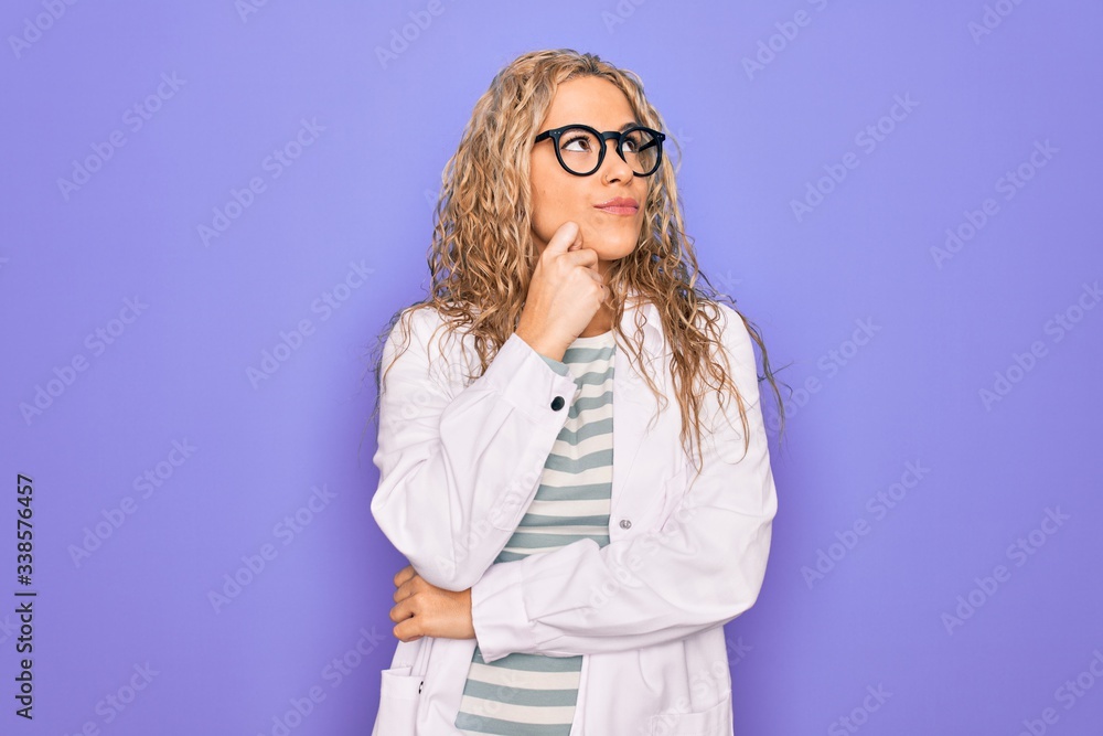 Young beautiful blonde scientist woman wearing coat and glasses over purple background with hand on chin thinking about question, pensive expression. Smiling with thoughtful face. Doubt concept. Young beautiful blonde scientist woman wearing coat and glasses over purple background with hand on chin thinking about question, pensive expression. Smiling with thoughtful face. Doubt concept.
