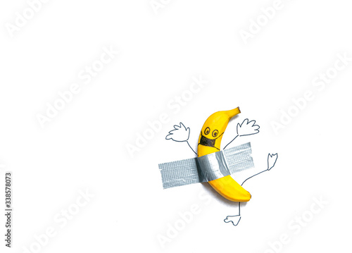 A banana in a painted protective mask glued with tape. Concept: be at home, take care of life. In the coronavirus epidemic, stay home.
