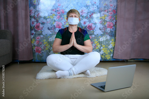 Woman 50 years old taking yoga lessons online and practicing at home while quarantine. The concept of a healthy lifestyle, well-being, safety during the coronavirus pandemic, the search for a new hobb photo