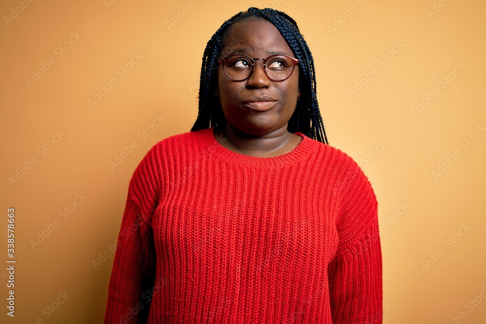 African american plus size woman with braids wearing casual sweater over yellow background smiling looking to the side and staring away thinking. African american plus size woman with braids wearing casual sweater over yellow background smiling looking to the side and staring away thinking.