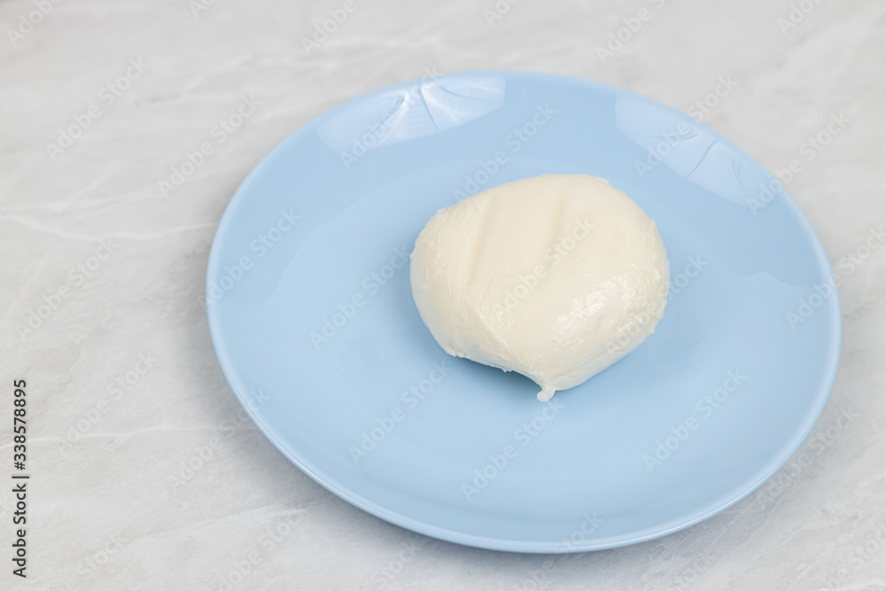 Mozarella cheese served on the blue plate above white marble table Mozarella cheese served on the blue plate above white marble table