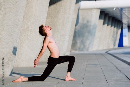 Young man performing joint movement exercise inspired by yoga, outdoors.