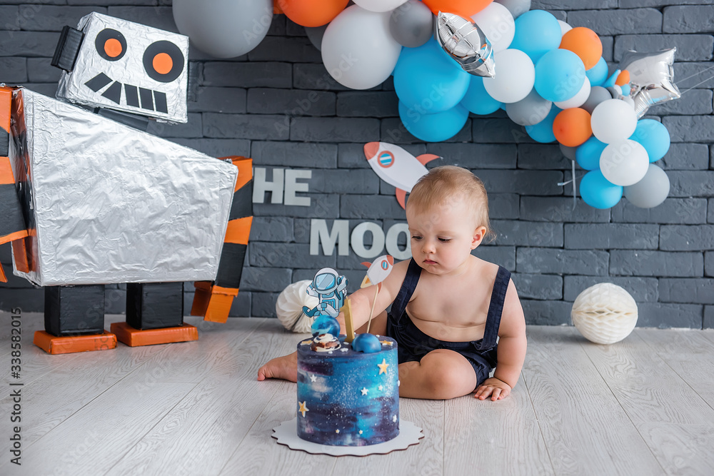 Naklejka premium Little boy celebrates his first birthday. Space design with a robot and stars, many colorful balloons.