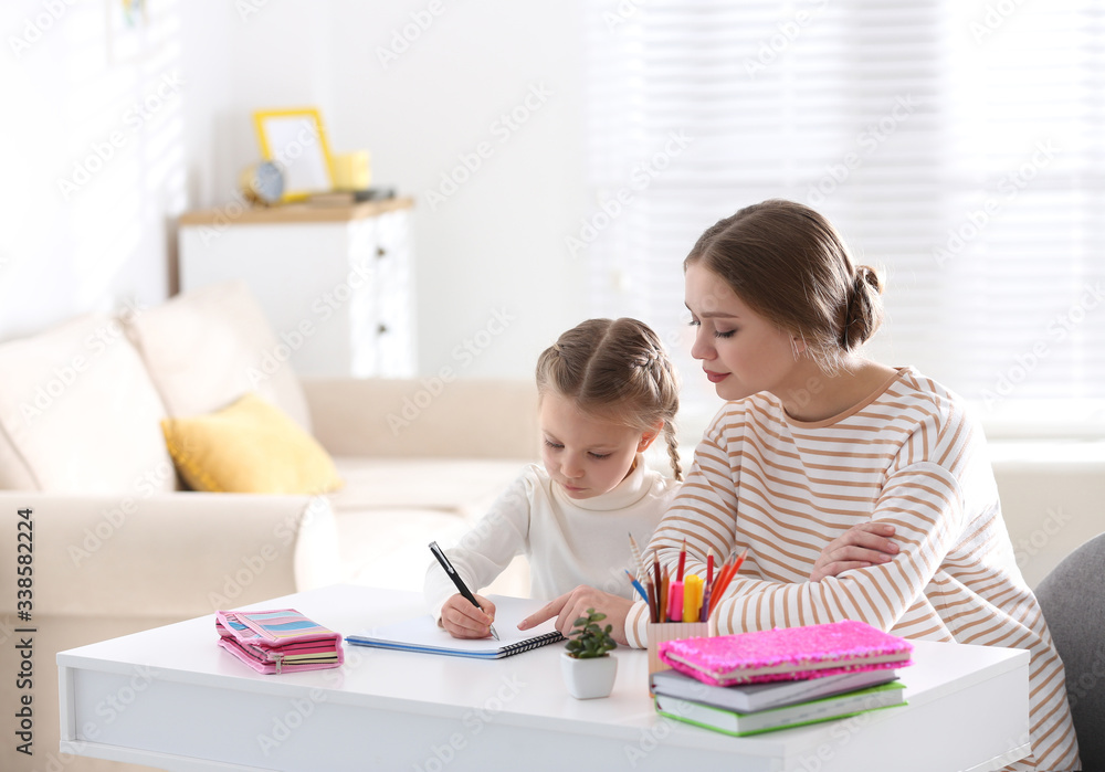 Woman helping her daughter with homework at table indoors Woman helping her daughter with homework at table indoors