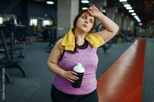 Overweight woman drinks diet cocktail in gym