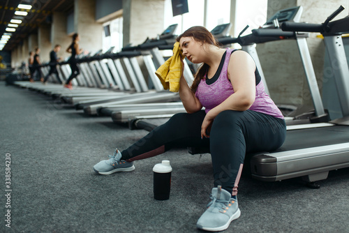 Tired overweight woman sitting on treadmill in gym photo