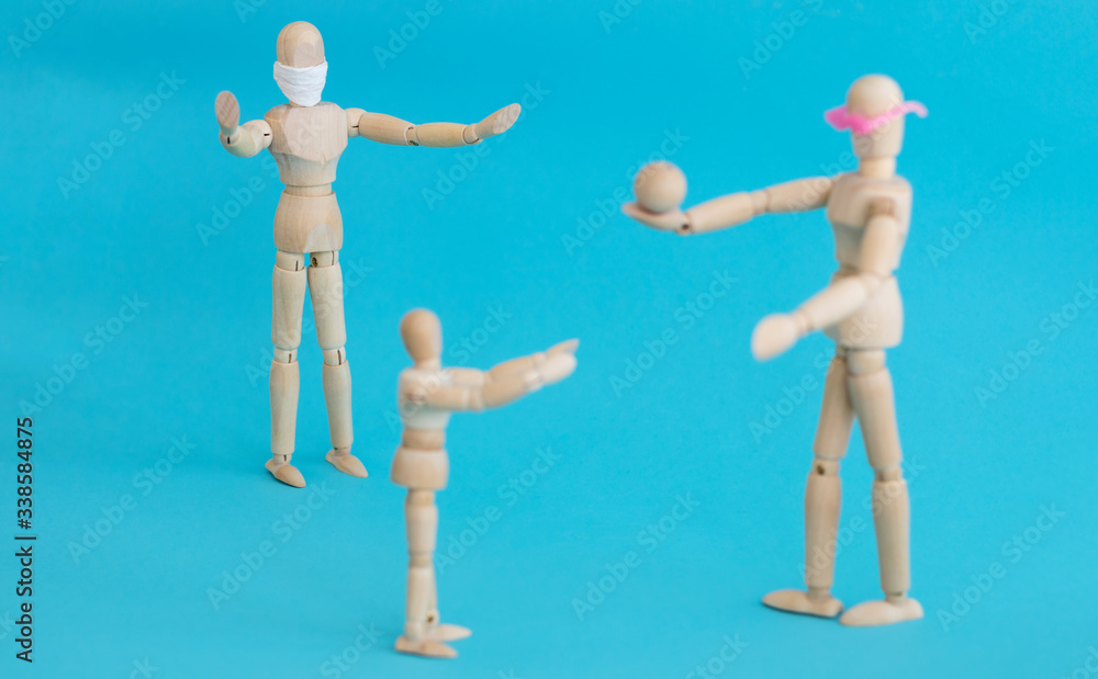 Concept - ban on ball games with children during quarantine. Group of wooden little men mannequins. A man in a protective medical mask prohibits others from playing actively. Social distance. Concept - ban on ball games with children during quarantine. Group of wooden little men mannequins. A man in a protective medical mask prohibits others from playing actively. Social distance.