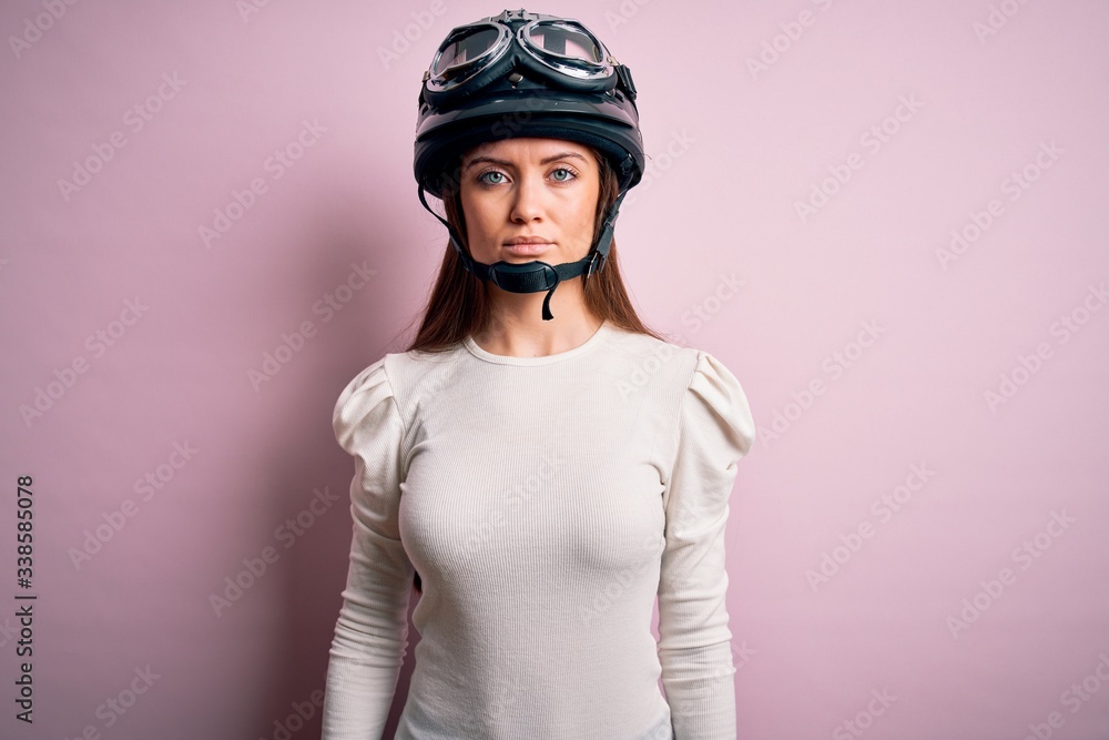 Young beautiful motorcyclist woman with blue eyes wearing moto helmet over pink background Relaxed with serious expression on face. Simple and natural looking at the camera. Young beautiful motorcyclist woman with blue eyes wearing moto helmet over pink background Relaxed with serious expression on face. Simple and natural looking at the camera.
