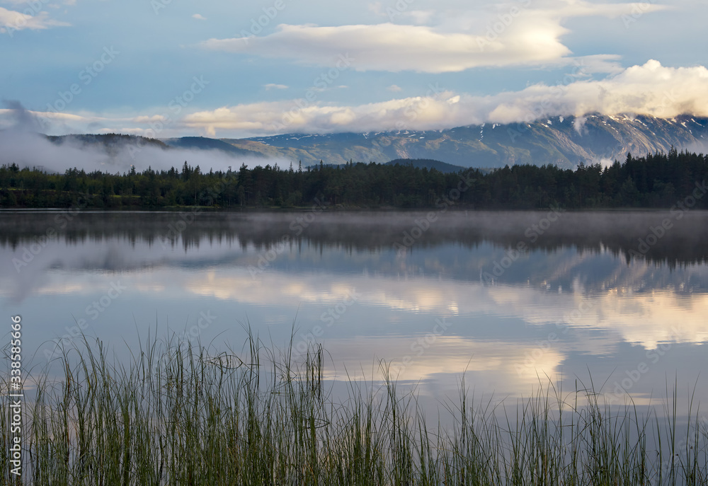 Morning. Dawn. Sky and clouds are reflected on the surface of the water. In the distance, the opposite shore of the lake and a mountain range are visible. Morning. Dawn. Sky and clouds are reflected on the surface of the water. In the distance, the opposite shore of the lake and a mountain range are visible.