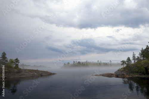 The bay, surrounded on two sides, rocky shores. In the distance, through heavy fog, you can see the neighboring island and access to the lake. Lead heavy sky.