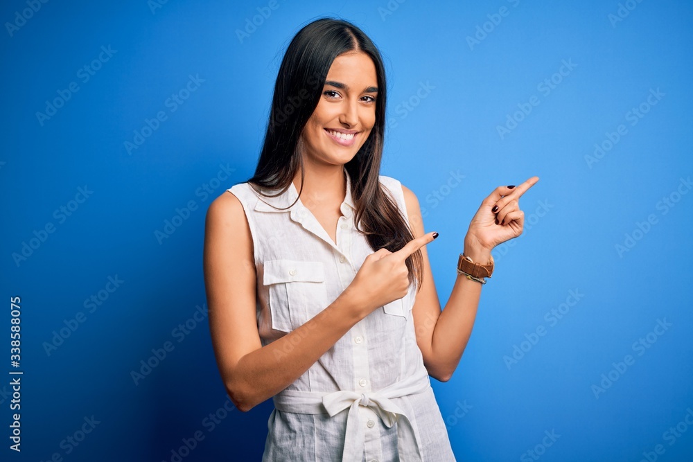 Young beautiful brunette woman wearing casual dress over isolated blue background smiling and looking at the camera pointing with two hands and fingers to the side. Young beautiful brunette woman wearing casual dress over isolated blue background smiling and looking at the camera pointing with two hands and fingers to the side.