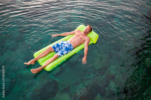 Overhead full length view of man relaxing on a green inflatable lilo floating on the water