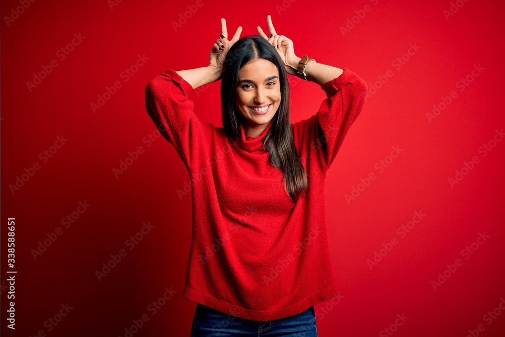 Young beautiful brunette woman wearing casual sweater over isolated red background Posing funny and crazy with fingers on head as bunny ears, smiling cheerful Young beautiful brunette woman wearing casual sweater over isolated red background Posing funny and crazy with fingers on head as bunny ears, smiling cheerful
