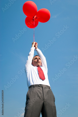 Nervous businessman holding onto a bunch of bright red balloons getting carried away into bright blue sky © PeskyMonkey