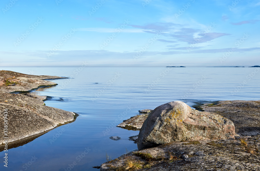 Landscape. Wildlife. Lake Ladoga. Summer. Bay with a narrow channel divided the island into two parts. On the right we see a large stone. Beautiful blue sky with light clouds.