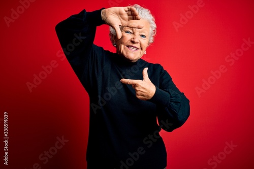 Senior beautiful woman wearing casual sweater standing over isolated red background smiling making frame with hands and fingers with happy face. Creativity and photography concept.