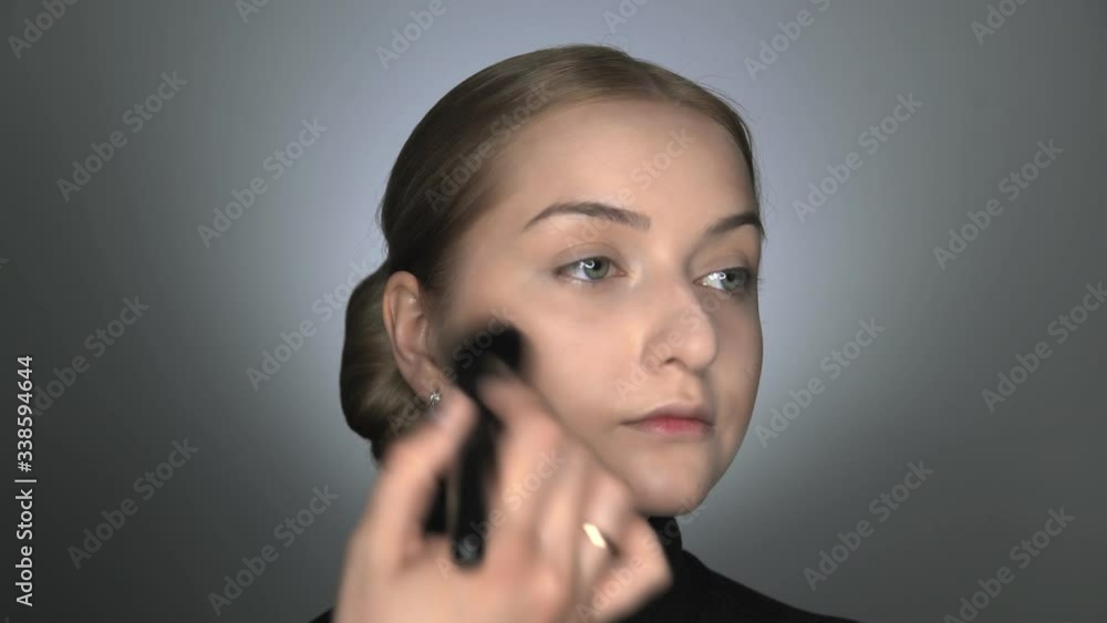 Make-up artist making professional make-up for young woman in beauty studio. Make up Artist applies powder with a big brush Make-up artist making professional make-up for young woman in beauty studio. Make up Artist applies powder with a big brush