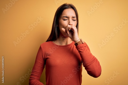 Young beautiful brunette woman wearing casual t-shirt standing over yellow background feeling unwell and coughing as symptom for cold or bronchitis. Health care concept.