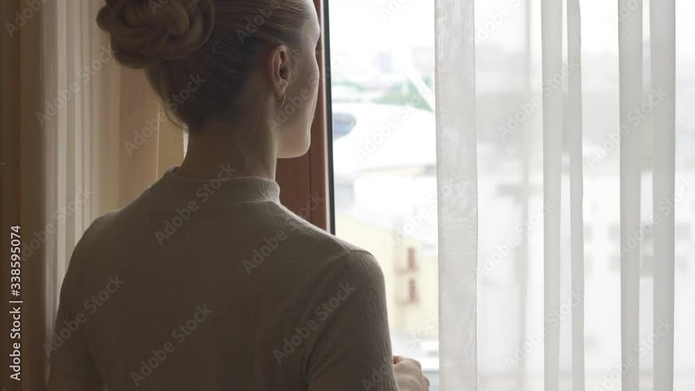 Businesswoman at a hotel by window looks out onto the street and drinks coffee Businesswoman at a hotel by window looks out onto the street and drinks coffee
