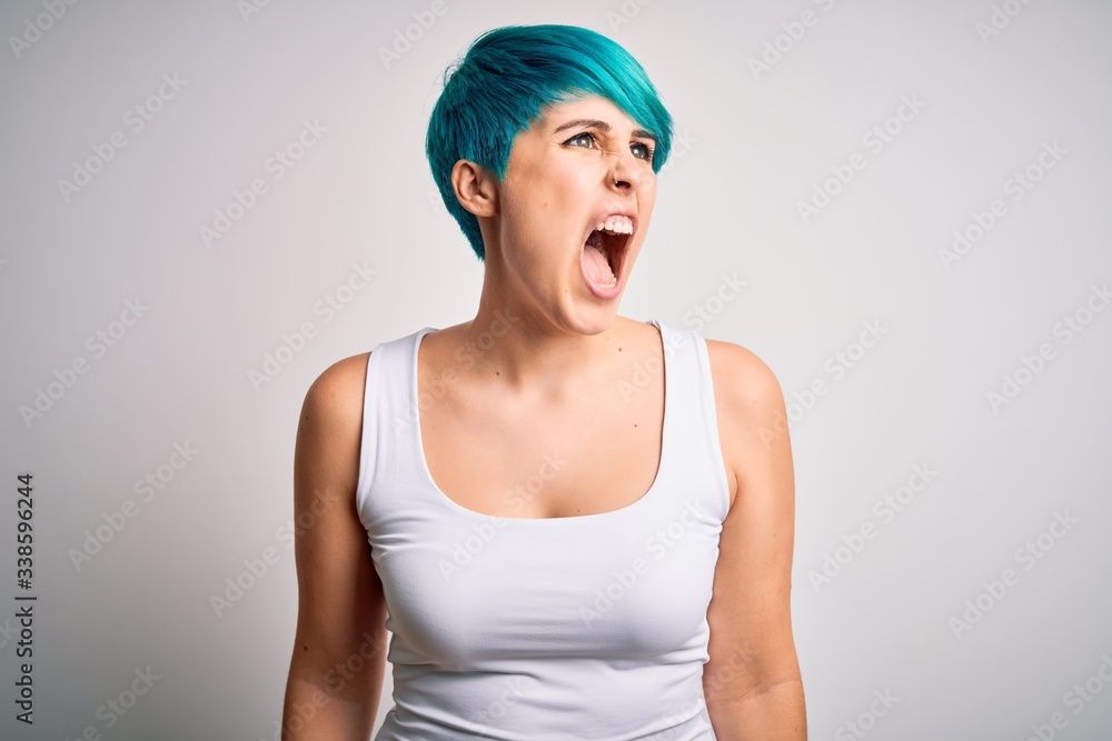 Young beautiful woman with blue fashion hair wearing casual t-shirt over white background angry and mad screaming frustrated and furious, shouting with anger. Rage and aggressive concept. Young beautiful woman with blue fashion hair wearing casual t-shirt over white background angry and mad screaming frustrated and furious, shouting with anger. Rage and aggressive concept.