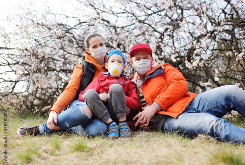 a young family-mother, father and young son in medical masks and respirators against the background of spring apricot blooms during the covid-19 coronavirus pandemic