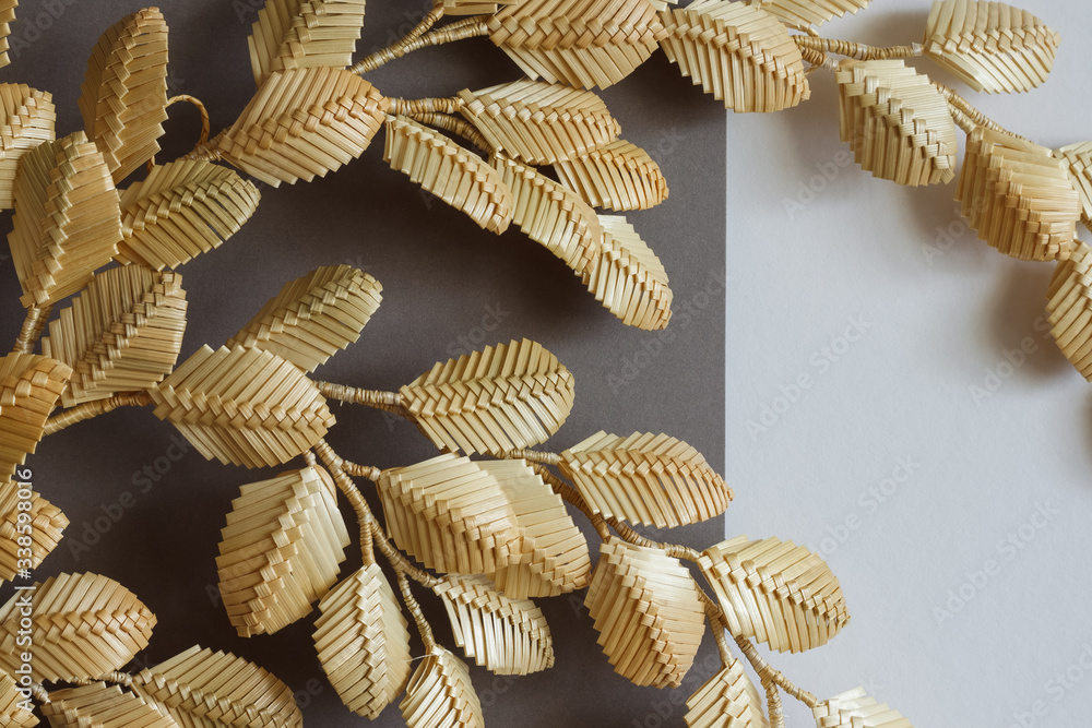The branch with leaves is made of straw. Straw wall decoration. The products are made of straw. Decoration of straw on a gray white background The branch with leaves is made of straw. Straw wall decoration. The products are made of straw. Decoration of straw on a gray white background