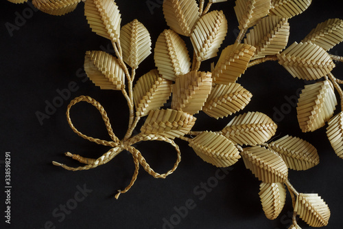 The branch with leaves is made of straw. Straw wall decoration. The products are made of straw. Decoration of straw on a dark background