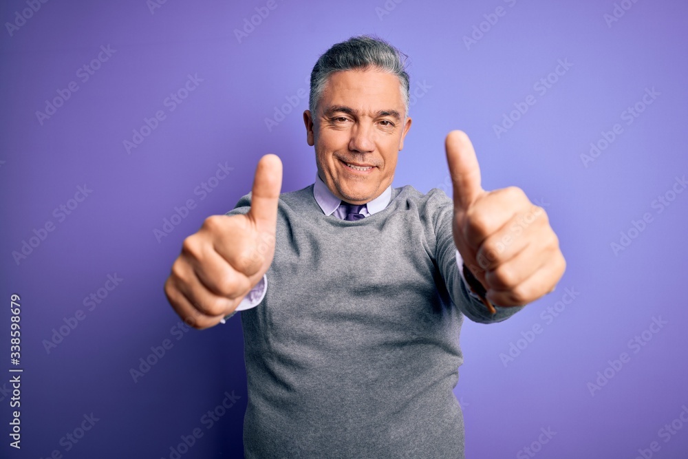 Middle age handsome grey-haired man wearing elegant sweater over purple background approving doing positive gesture with hand, thumbs up smiling and happy for success. Winner gesture. Middle age handsome grey-haired man wearing elegant sweater over purple background approving doing positive gesture with hand, thumbs up smiling and happy for success. Winner gesture.