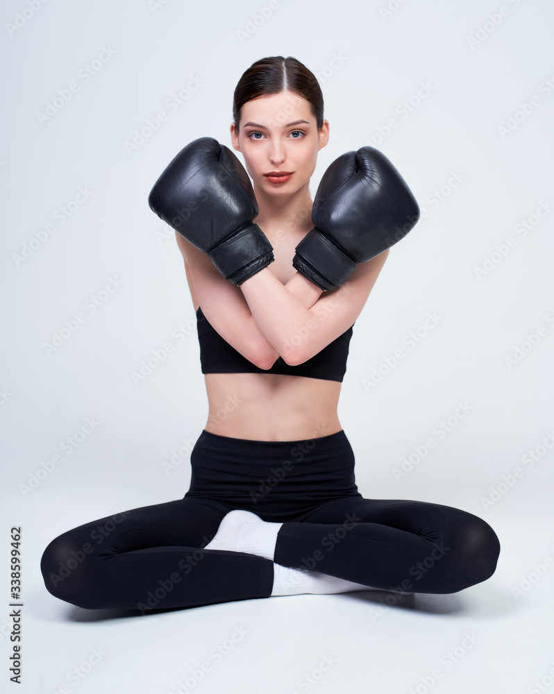 A young woman in black boxing gloves sits on a white background. A young woman in black boxing gloves sits on a white background.