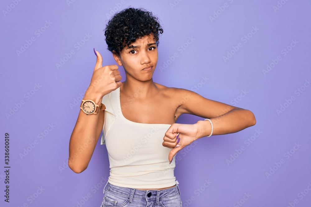 Young beautiful african american afro woman wearing casual t-shirt over purple background Doing thumbs up and down, disagreement and agreement expression. Crazy conflict